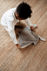 A young child with curly hair and a white shirt picks up the Senger Naturwelt Stuffed Animal - Large Manta Ray from a woven, tan-colored rug.