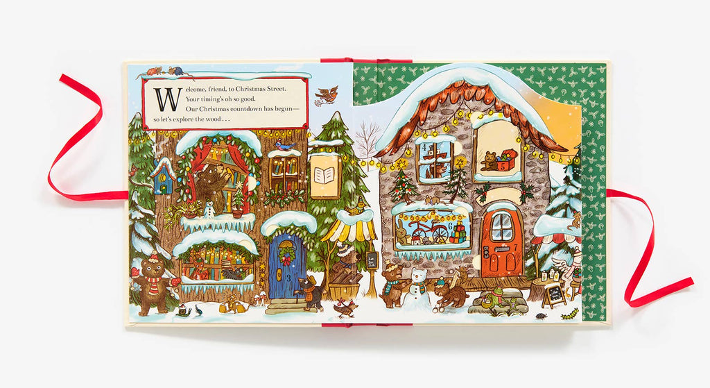 The illustrated children’s book "Christmas is Coming to Town!" shows snow-covered houses, festive trees, Brown Bear Wood animals, and Christmas lights. A text box reads, "Welcome, friend, to Christmas Street..." framed by red ribbons.
