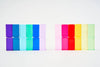 Two side-by-side grids of colorful translucent rectangles, similar to Bauspiel Luminous Blocks - 24 Piece, are set against a light background. The left grid features shades of purple, blue, and green; the right displays pink, red, yellow, and green hues.
