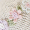 Close-up of Cuddle + Kind Emma The Mouse’s knitted beige fabric, adorned with pastel pink, white, and lavender crocheted flowers and green leaves—crafted from hypoallergenic materials for comfort and safety.
