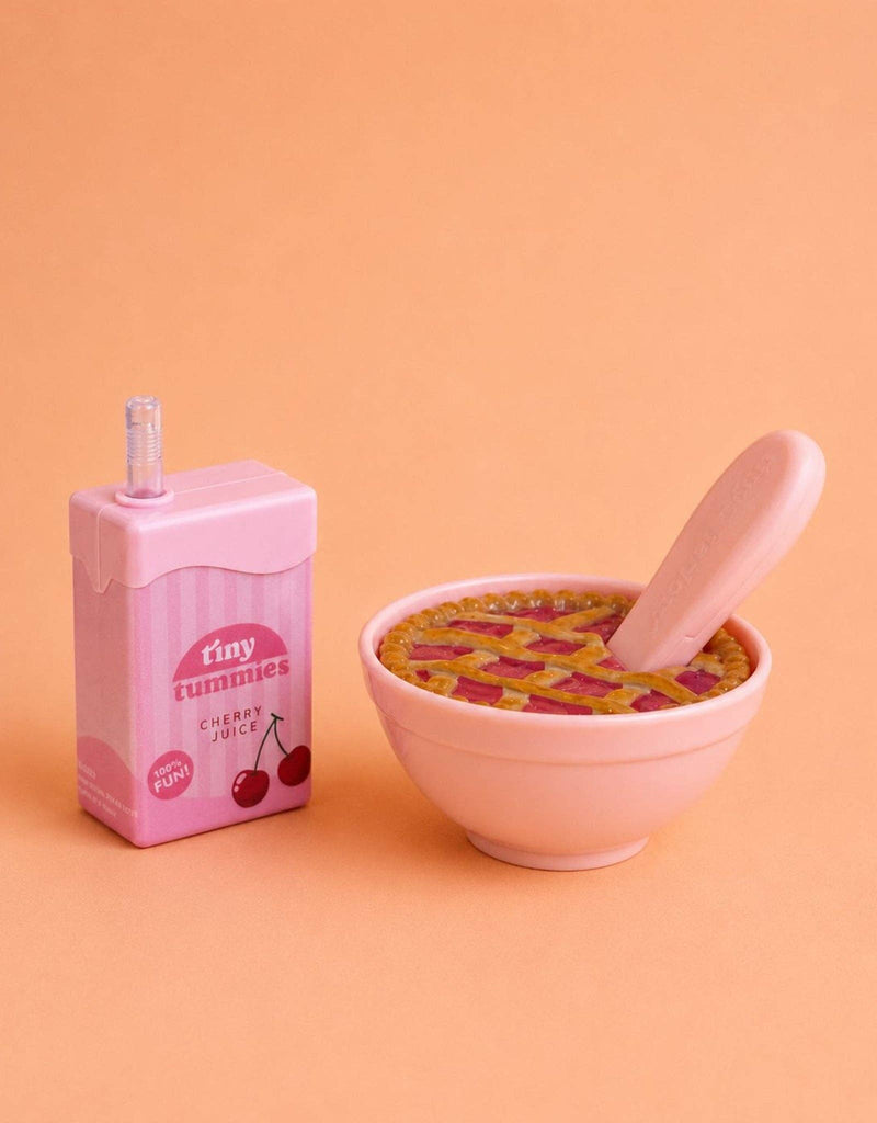 The Tiny Tummies Set - Cherry Pie Bowl and Juice Box features a pink bowl filled with a toy cherry pie and spoon, next to an interactive juice box labeled “cherry juice.”