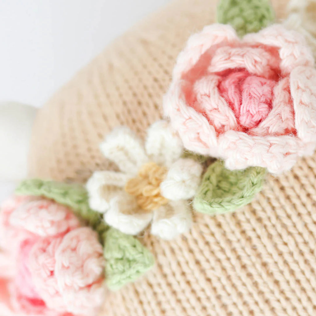 Close-up of Cuddle + Kind Amelia The Cow, featuring beige knitted fabric with pink and white crocheted flowers and green leaves—detailed stitches and soft textures make it ideal for handmade, sustainable dolls or toys.