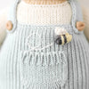 Close-up of a hand-knit Cuddle + Kind Charlie The Honey Bear outfit in light blue with a front pocket, featuring an embroidered bee and a white stitched design above the pocket.