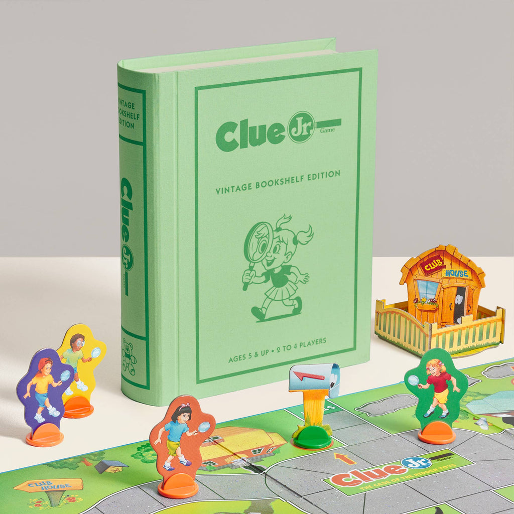 A green Clue Jr. Vintage Bookshelf Edition board game box sits behind a game board featuring illustrated character pawns, a mailbox, and a cardboard clubhouse.