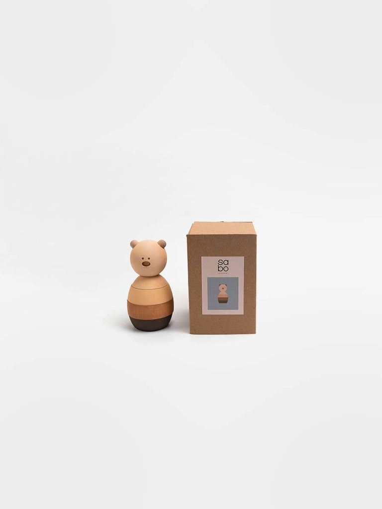 The Sabo Concept Bear Stacker - Beige, a small wooden toy with a round body, stands beside its brown box displaying its image, all set against a plain white background.