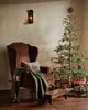 Coral & Tusk Christmas Tree Sled Pillow featuring embroidered animals on a rectangular decorative pillow, resting on a brown wingback chair next to a decorated Christmas tree.