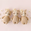 Three Cuddle + Kind Baby Pony plush toys—beige with white manes and tails—are hand-knit from soft Peruvian cotton yarn, arranged side by side on a pale pink background surrounded by small white flowers.