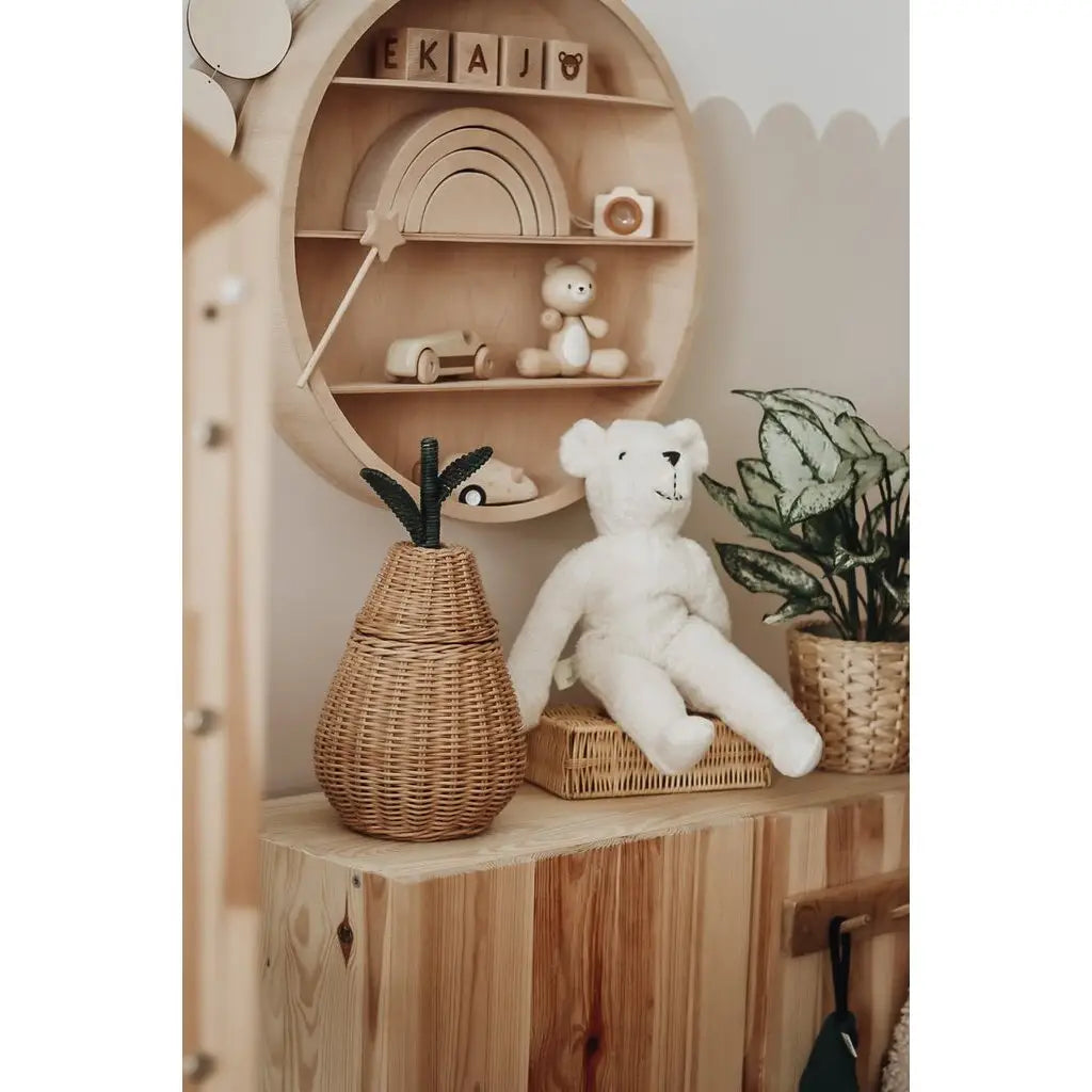 A cozy wooden shelf displays a wicker basket, a Senger Naturwelt Stuffed Animal - White Bear, a potted plant, and a circular wall shelf with wooden toys, blocks, and a small figurine in a softly lit minimalist kids’ room.