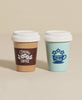 The Wooden Coffee And Tea Cups Set includes two toy cups with white lids—one brown with a “Fresh Coffee” logo and coffee bean graphic, and one light blue with a teacup and floral design—ideal for imaginative or role play.
