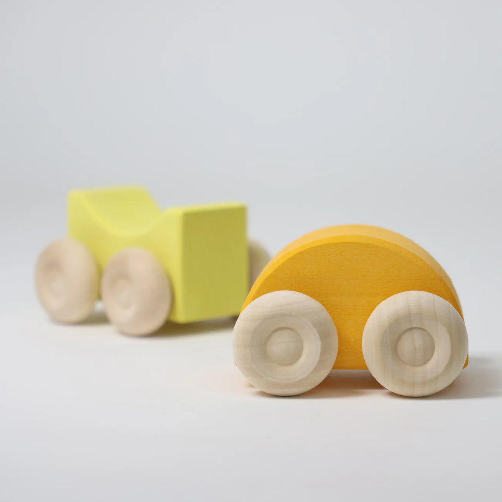 A Grimm's Stacking Car in yellow, with rounded shapes and natural wood wheels, rests on a white surface—perfect for color matching play.