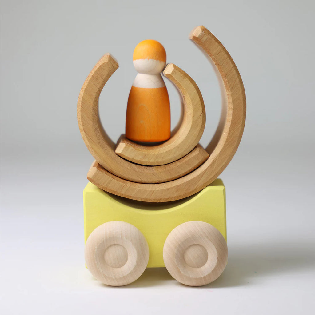 A wooden toy figure stands on yellow wheels, surrounded by three stacked Grimm's Stacking Cars - Yellow arches against a plain light background.