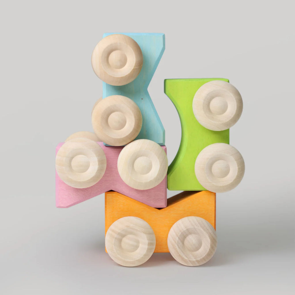 Four colorful wooden blocks—blue, green, pink, and orange—stacked with two round wheels each. These stacking toys resemble Grimm's Stacking Cars - Blue, shown against a plain gray background.