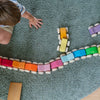 A child sits on a green carpet, playing with Grimm’s Stacking Cars – Purple (coming soon), a colorful wooden stacking toy from Germany, as they reach out to arrange the vibrant cars in a playful curve.