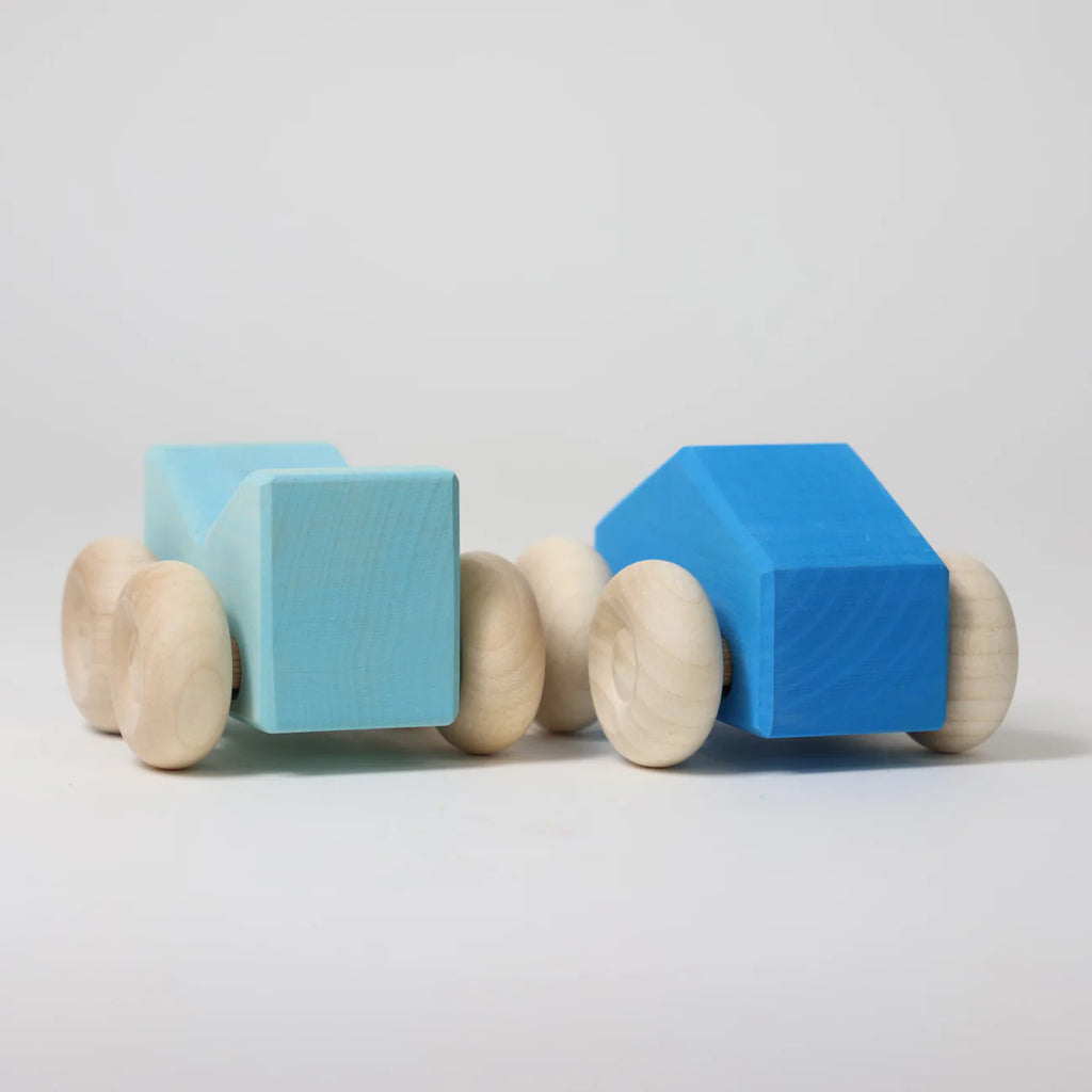 Two Grimm's Stacking Cars - Blue, one light blue and rectangular, the other dark blue and angular, both with natural wooden wheels, are displayed against a plain white background.