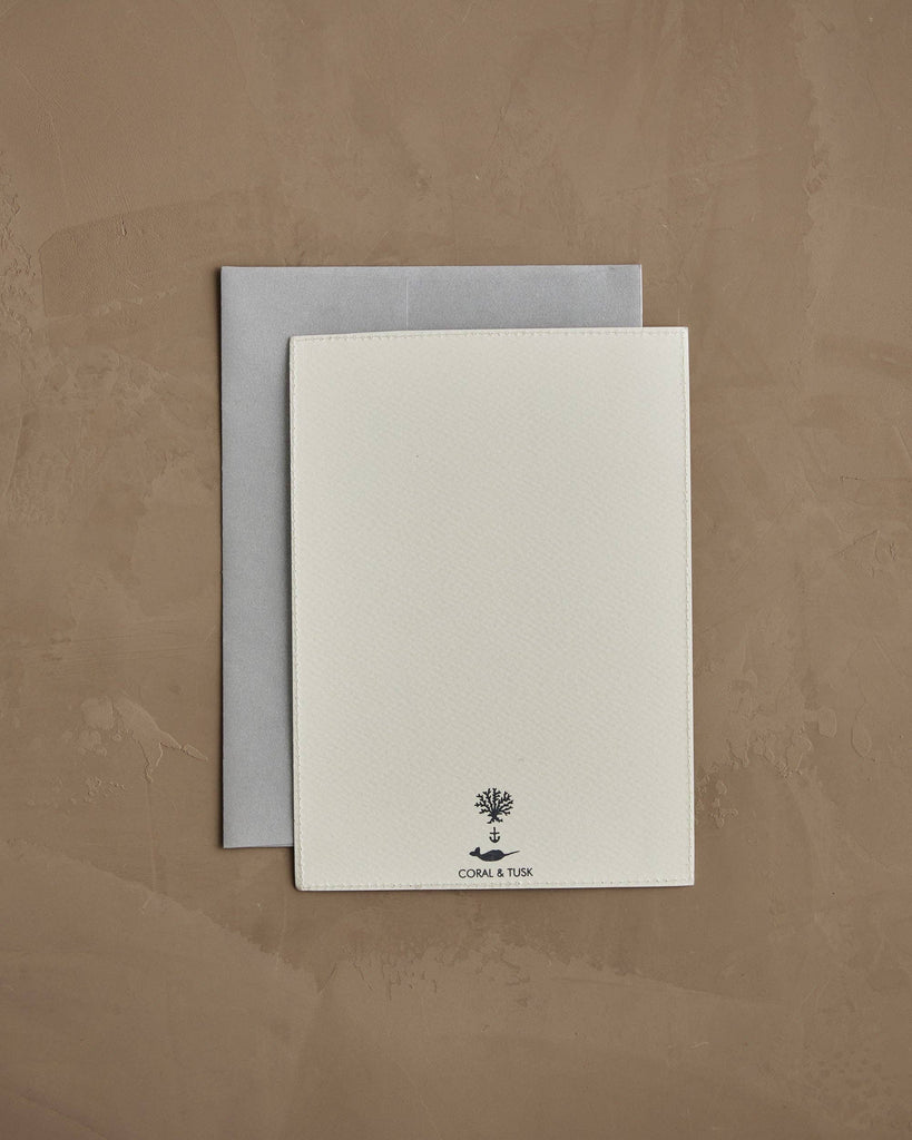 The Coral & Tusk Fox Mama Card—a white textured keepsake with a small tree logo and "CORAL & TUSK" at the bottom—comes atop a gray envelope on a light brown surface, making it an ideal gift for new parents.