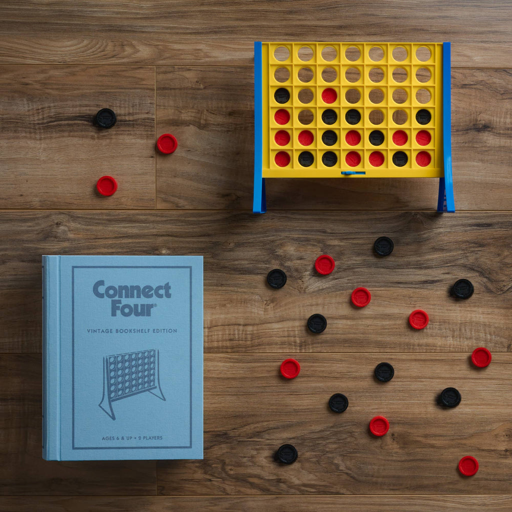 A partially played Board Game: Connect 4 Vintage Bookshelf Edition sits on a wooden surface, red and black discs scattered nearby. Next to it is a light blue box labeled with the game's name.