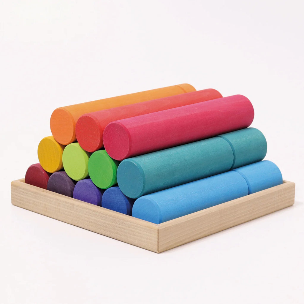 Grimm’s Large Building Rollers Rainbow arranged in a pyramid shape of twelve rainbow-colored wooden cylinders inside a square wooden tray, perfect for color sorting.