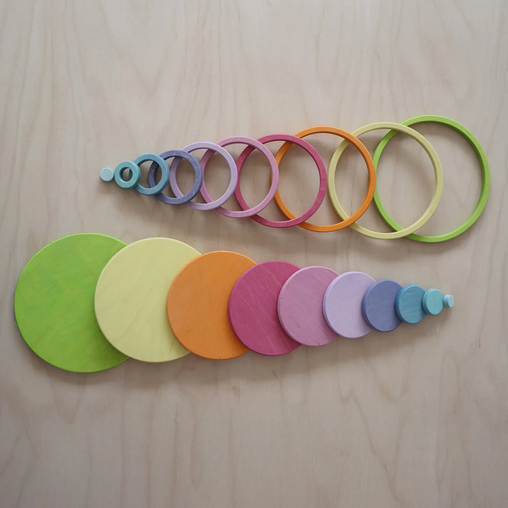 The Grimm's Concentric Circles and Rings Building Set - Pastel features colorful wooden circles and rings in various sizes, neatly arranged from smallest to largest on a light wood surface, perfect for creative building or balance play.