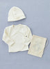 A neatly arranged display of a cream-colored Baby Cap & Cardigan made from organic cotton. The set includes a long-sleeved wrap-around cardigan with side snap closures, a matching baby hat, and a small beige drawstring bag with an illustration and text. The items are on a light blue background.