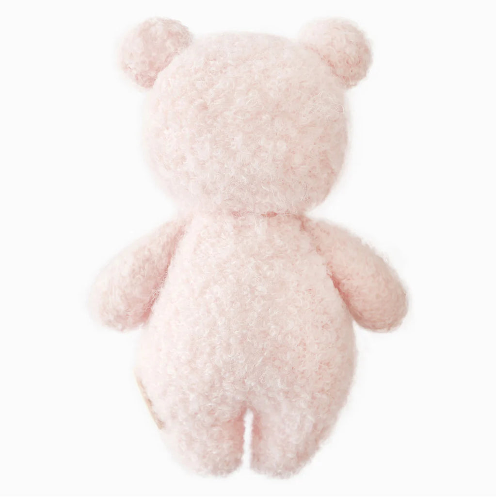 The Cuddle + Kind Baby Bouclé Bear - Strawberry is a soft, fluffy, light pink teddy bear made from Peruvian alpaca yarn. Shown from the back on a white background, it features round ears, short arms and legs, and no visible facial features.