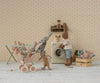 Four plush rabbits are in a vintage laundry room. One pushes two little ones in the Maileg Stroller, Micro - Powder, while another stands by a toy washing machine. Clothes hang on a drying rack nearby.