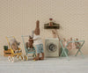 Two stuffed rabbits do laundry in a micro, vintage-style room. One rabbit pushes a Maileg Stroller, Micro - Yellow with a smaller bunny inside, while laundry dries on a rack and a toy washing machine adds to the cozy, whimsical scene.