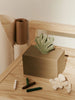 A wooden table displays the Ferm Living Hand Carved Wooden Harbour Box - Coral, a rectangular beige storage box with a carved handle and green leaf décor. Nearby are rolled papers, white coral, and pastel sticks in a minimalist FSC aspen wood setting.