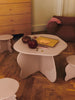 A small beige kids’ table with art supplies, apple, bowl, and the Ferm Living Apple Money Bank (ships in one week) on top, surrounded by matching stools—perfect for children’s room decor with a dresser and cushioned chair nearby.