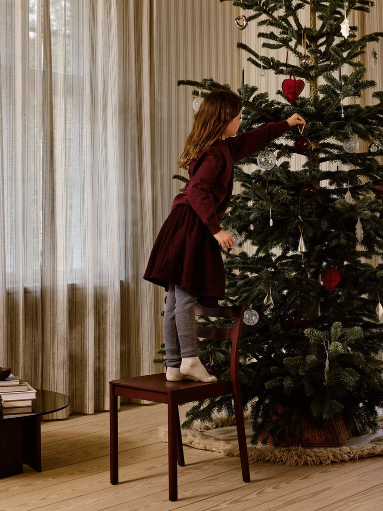 A child stands on a chair to hang silver Ferm Living Oak Leaf Ornaments - Set of 4 - Silver on a decorated tree.