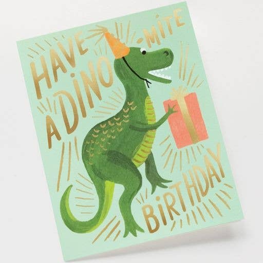 The Dino-mite Birthday Card shows a green dinosaur in an orange party hat holding a gift with "Have a dino-mite birthday" in playful letters. It includes a metallic gold envelope and has a blank interior for your message.
