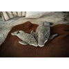 Two Senger Naturwelt Cuddly Animal - Dolphin toys made from sustainable materials rest side by side on a brown textured blanket, with neutral knit and striped bedding in the background.