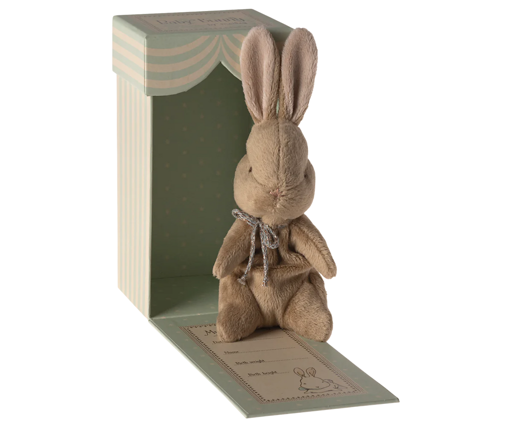 The Maileg My First Bunny - Brown is a soft plush bunny with a silver bow, nestled in a pastel green polka dot gift box featuring scalloped edges, “My first bunny” text, and an adorable bunny illustration on the base.