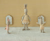 Three Maileg Rabbit, Size 1 - Classic - Ballet Suit and Skirt - Cream toys in pastel tutus stand on a textured surface before a patterned yellow wall with three small mirrors, striking playful poses as if mid-dance.