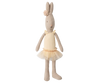 The Maileg Rabbit, Size 1 - Classic - Ballet Suit and Skirt - Cream is posed like a ballet dancer, wearing a yellow headband with a pompom and a yellow tulle tutu dress against a neutral striped background.