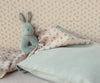 The Maileg Bunny Rattle Set - Mint rests on pastel floral bedding, complemented by wallpaper with delicate blue flowers. Made from soft cotton in pink and blue tones, the bedding creates a cozy and serene ambiance.