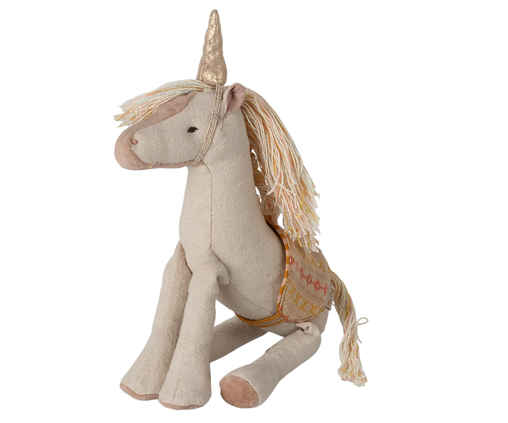 The Maileg Unicorn, Small is a plush kids toy featuring a beige body, gold horn, long cream and gold mane and tail, and an embroidered pink and gold saddle. This unicorn sits upright to spark any magical adventure.