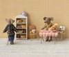 In a tiny kitchen, Maileg Mum Mouse, light brown in a plaid shirt and jeans, is by the bread shelf with mouse furniture. Across the room, another mouse in a cotton scarf sits at a red-checkered table with pies and a cloche. A teapot rests on the shelf. (Ships in one week.).