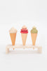 Three Handmade Ice Cream Cones with different colored scoops, painted with non-toxic water-based paint, displayed on a small wooden rack against a plain white background.