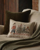 A Coral & Tusk Christmas Tree Sled Pillow on a sofa, featuring an embroidered linen design of a bear pulling a sled with a Christmas tree and two animals, surrounded by a throw and additional holiday decorative pillows.