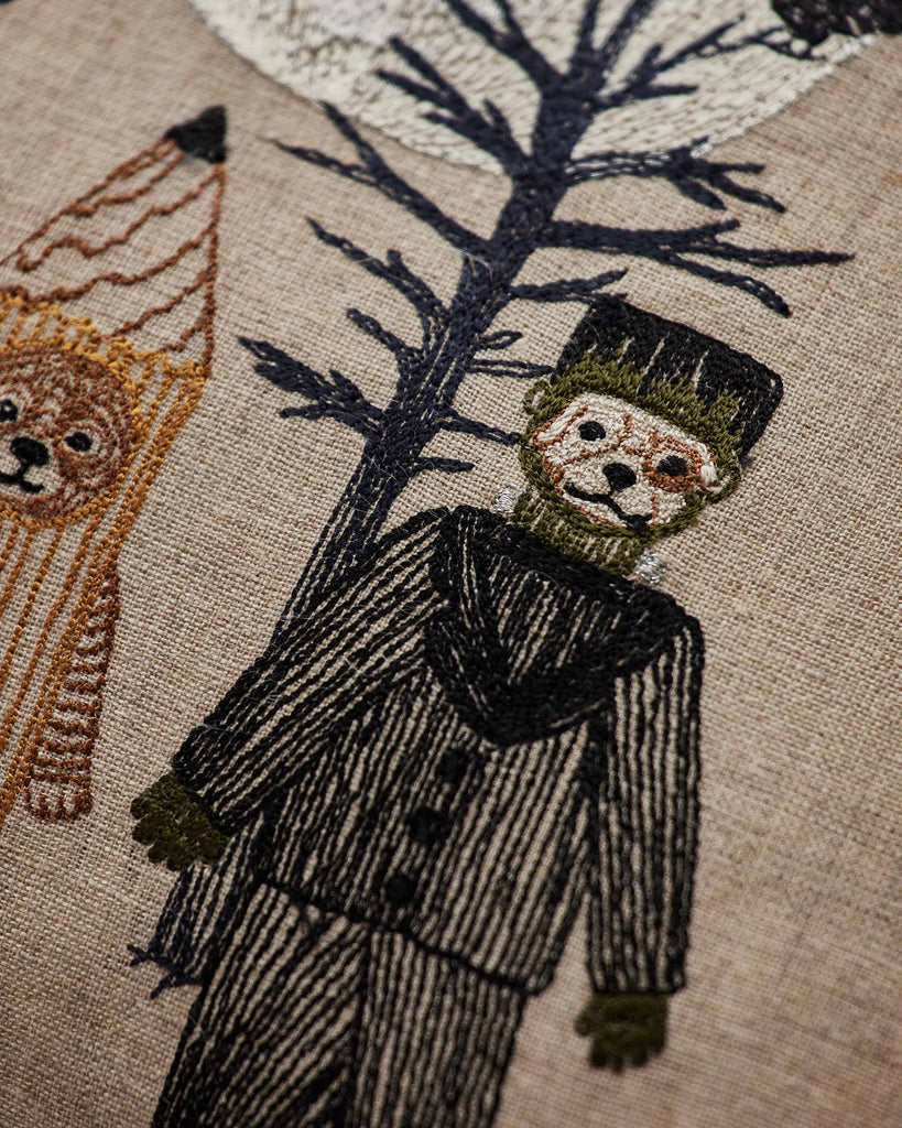 The Coral & Tusk Full Moon Masquerade Pillow features embroidered Halloween figures—a bear in stripes and a person in a dark costume by a blue tree—making it the perfect festive decor.