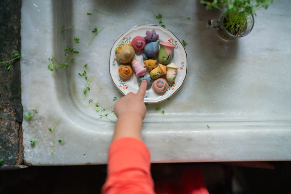 A child’s hand reaches for sweets on a marble surface, with green herbs, a glass cup, and the Grapat Play Set - Flower Meadow visible nearby.