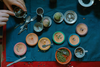 The Grapat Play Set - Dishes features a vibrant arrangement of seeds and spices in small bowls, wooden plates, and trays on a blue cloth. Hands use spoons and cups to sort, with scattered spoons and loose seeds creating a playful scene.