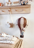 A small stuffed mouse sits in the Hot Air Balloon - Light Brown / Dark Brown, hanging in a cozy nursery with folded blankets, a toy airplane, and a wooden camera—perfect as a charming children’s room decoration.