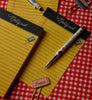 Two yellow Class Notes Notepads with “Notepad” printed at the top rest on a red checkered tablecloth. Each pad contains lined paper with convenient tear-off sheets. A pen and paper clips, including one labeled “Eraser” in pink, are also on the table.