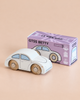 A small white classic wooden toy car with beige wheels, the No. 9 GT55 Betty | Made in England, sits beside its purple box labeled “GT55 BETTY” and “Limited Edition” on a light beige surface, evoking the nostalgic charm of a timeless toy perfect for imaginative play.