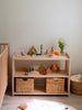 A wooden shelf displays the Sabo Concept Aviator Mouse among colorful toys and puzzles. Two woven baskets are below, a vase of flowers on top, with a crib and laundry basket in the bright, cozy room.