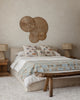 A cozy bedroom with a neutral palette features a bed with nautical accent pillows, including the Coral & Tusk Sailing Foxes Pillow, rustic wooden side tables and bench, woven lamps, and wicker wall art above the headboard.