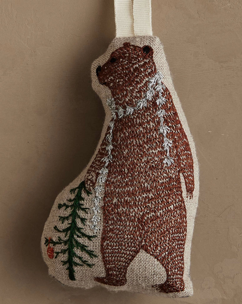 The Coral & Tusk Bear with Tinsel Ornament features an embroidered bear in a white scarf holding a pine branch with a red ornament—a delightful woodland accent for your Christmas home decor.
