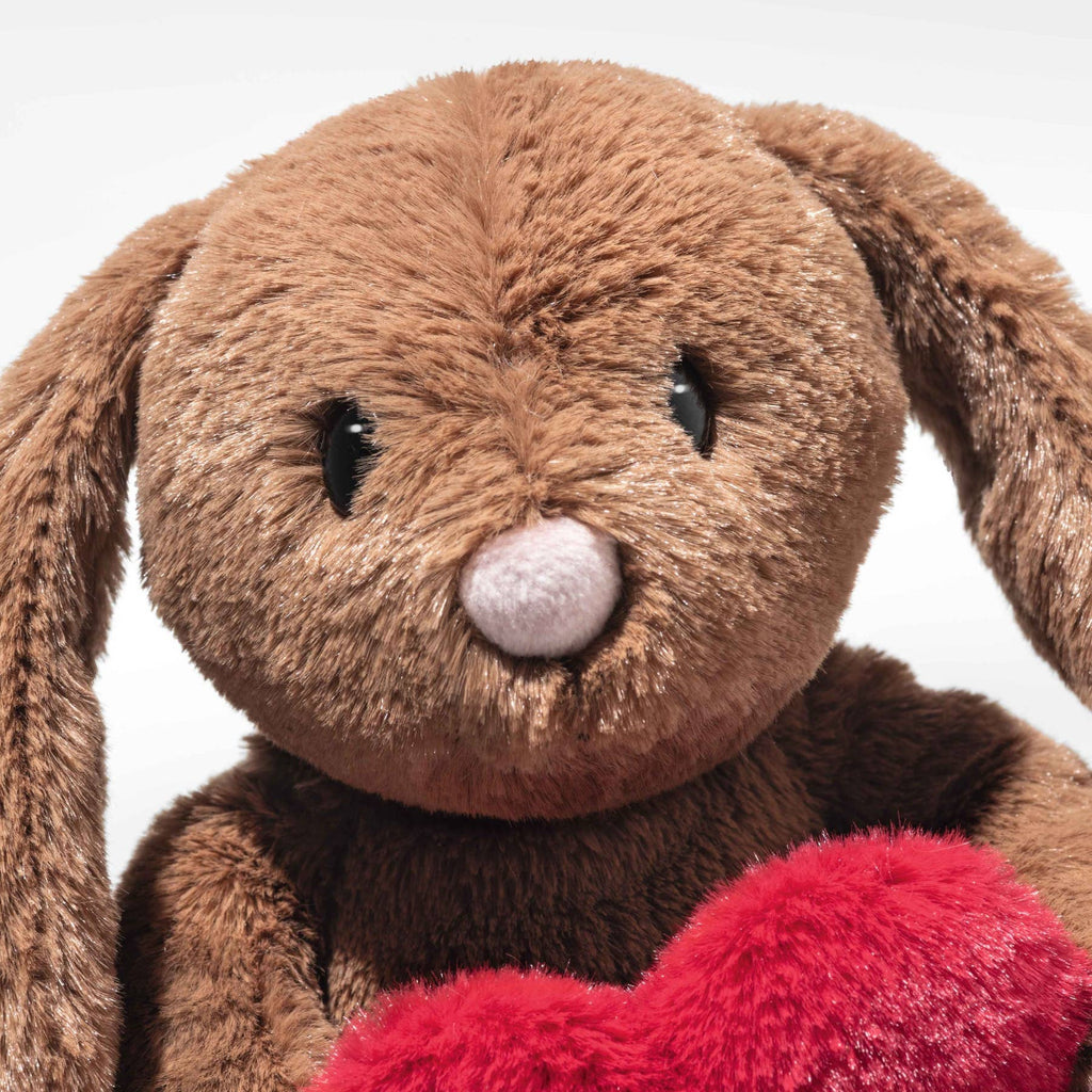 A close-up of the Steiff Hoppie Rabbit – Love plush toy with long floppy ears, black eyes, a pink nose, and a red heart—an ideal gift for Steiff fans—set against a plain white background.