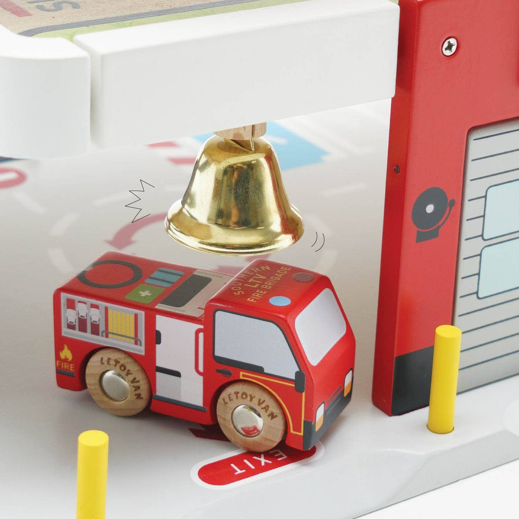 The Fire & Rescue Garage playset features a wooden toy fire engine under a gold bell beside a red building with a garage door and yellow bollards, sparking imaginative play and exciting adventures.